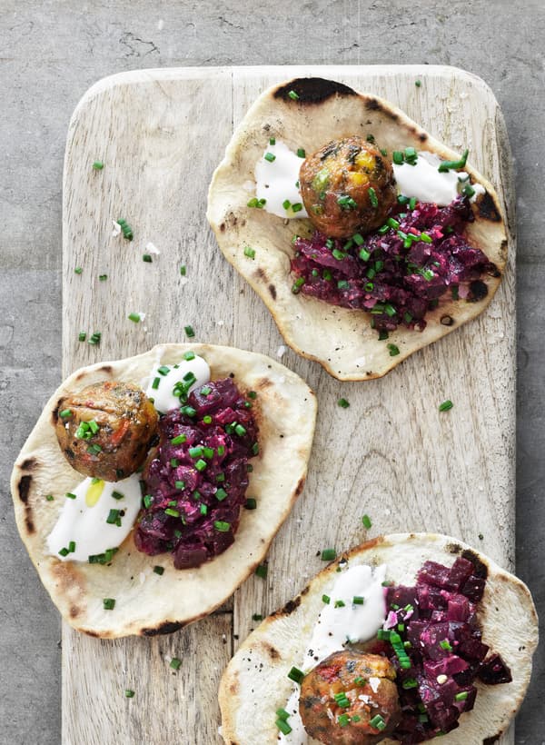 Roasted beet relish and veggie balls on naan bread garnished with yoghurt and chopped chives, served on a wooden board, seen from above.