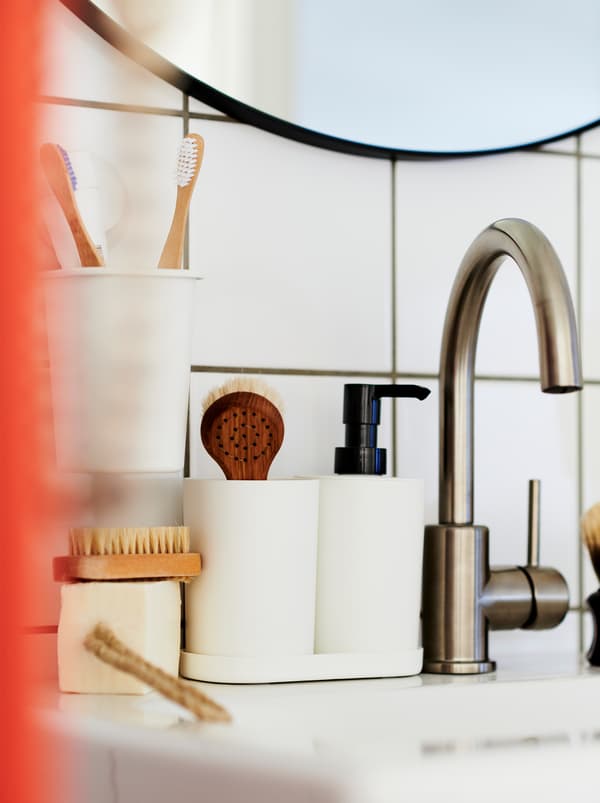 Robinet de apă într-o baie cu gresie și faianță albă cu un set de trei piese STORAVAN și accesorii așezate pe marginea lavoarului.