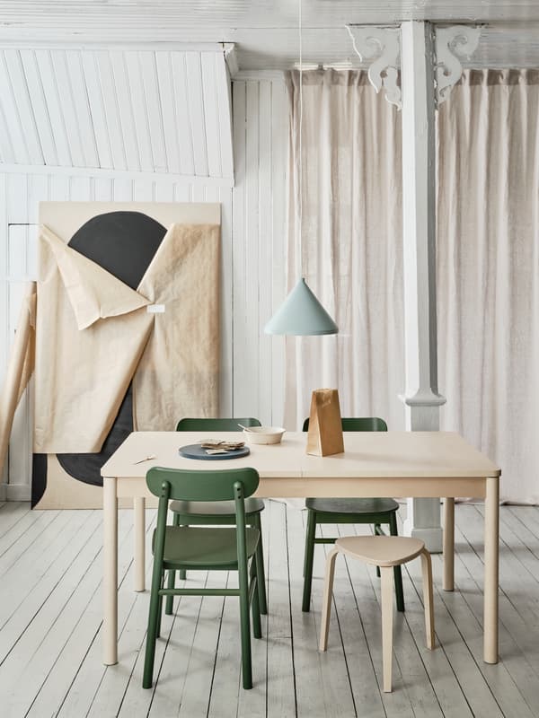 RÖNNINGE extendable table in light birch and rounded legs placed in a dining context with chairs around in a light room.