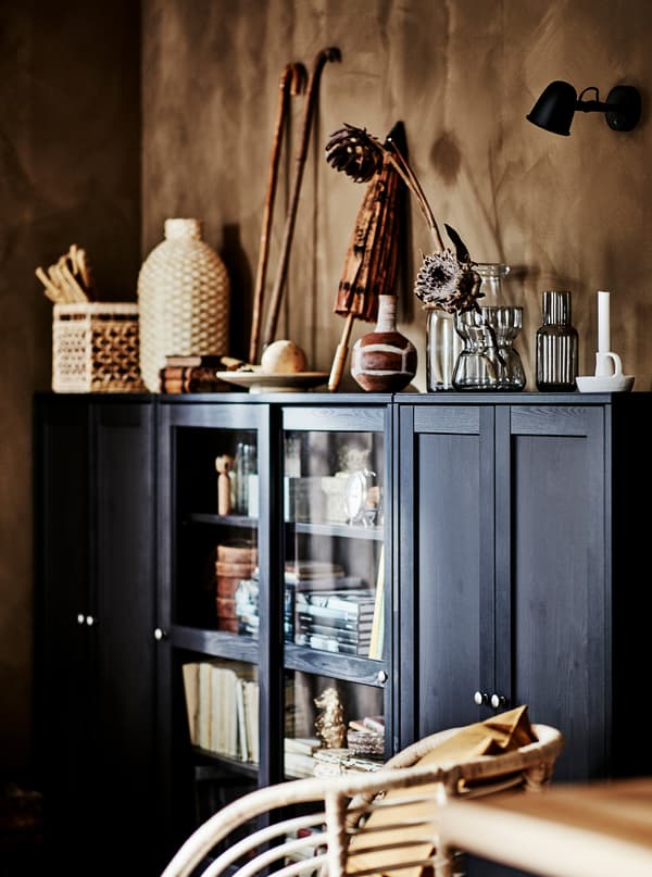 Roh obývacej miestnosti so širokou, tmavou skrinkou HAVSTA s umeleckými predmetmi z prírodných materiálov. 