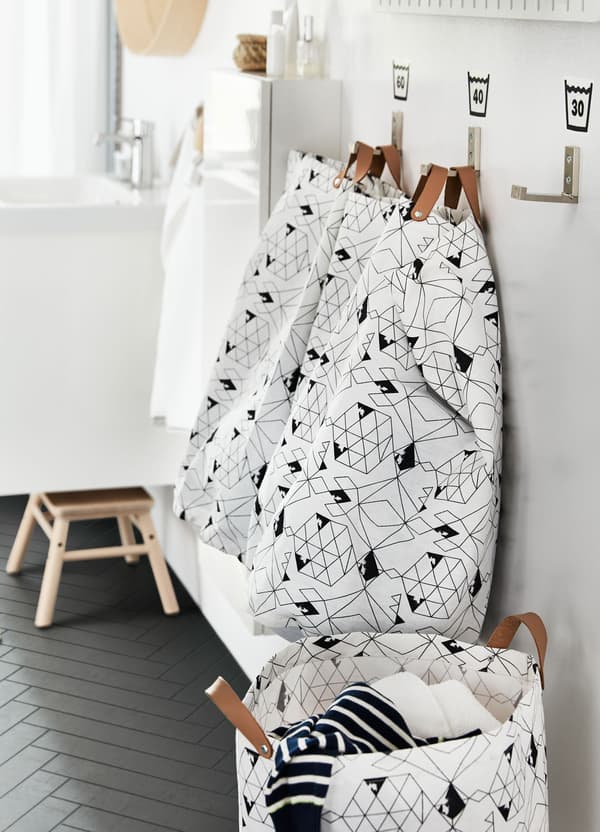 Ronde IKEA PLUMSA waszakken, met leren handgrepen en witte en zwarte geometrische motieven, aan haken.