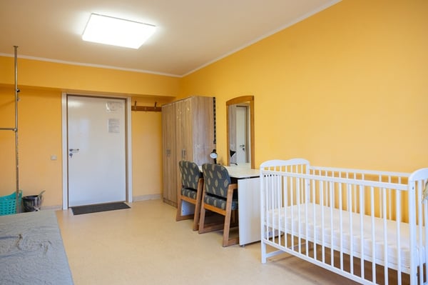 Room before renovation with a baby crib, wardrobe, and basic lighting.