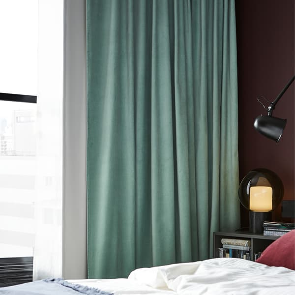Room darkening curtains in light green, a black wall lamp, a dark red cushion cover and a white quilt cover.