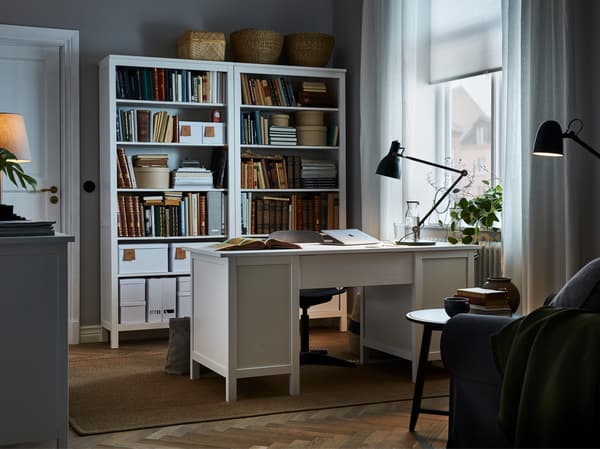 Room with a white desk placed centrally, matching tall bookcases behind the desk chair, and a green work lamp on the desk.