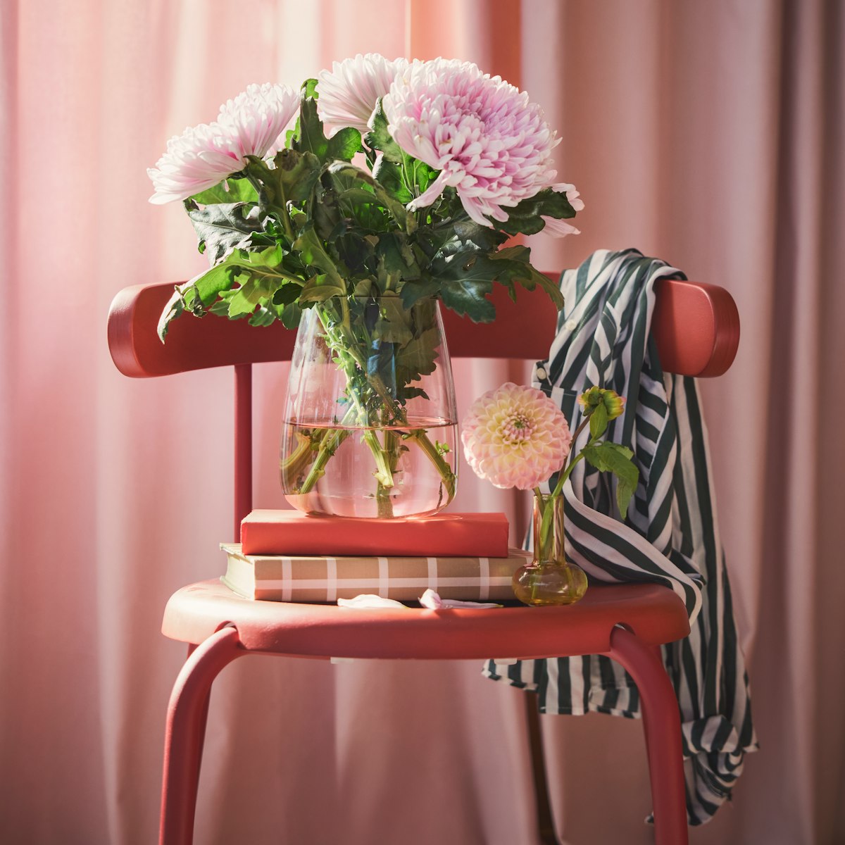 Roosade lilledega klaasvaas, mis on kujundatud dekoratiivse aktsendina, seisab maheda valgusega ruumis punasel toolil.