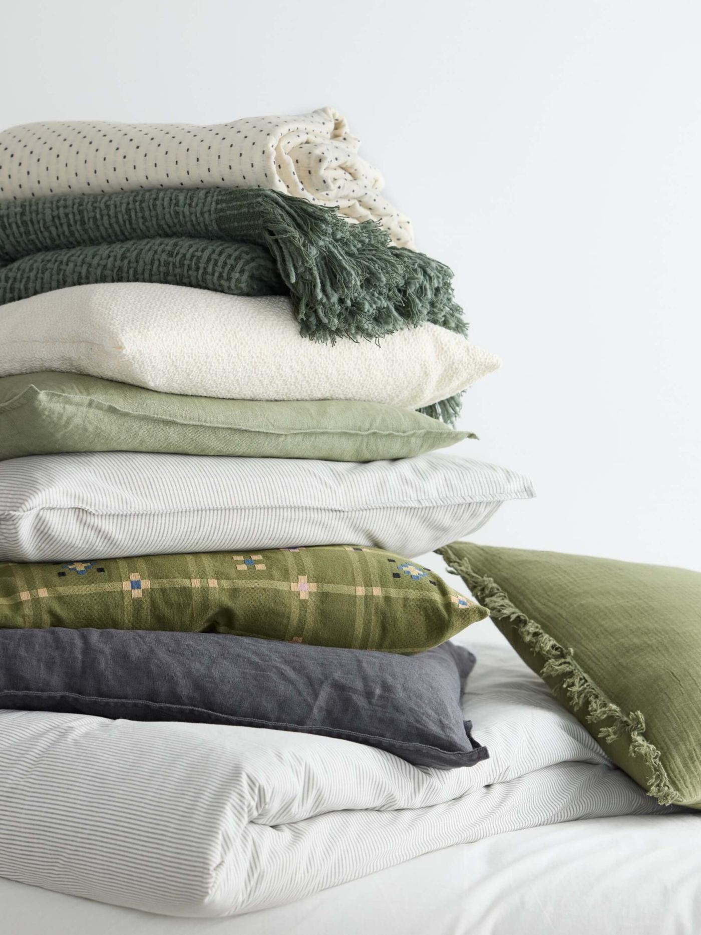 Ropa de cama en color verde, crema y gris apilada una encima de la otra.