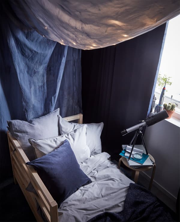 Ropa de cama y fundas de almohada ÄNGSLILJA. Una estructura de cama y un dosel de tejido azul oscuro y cortinas opacas.