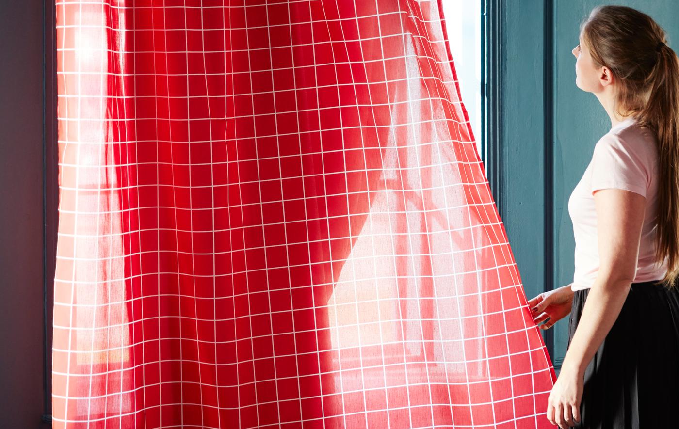 ผ้าม่านแบบบาง ROSALILL/รูซาลิล ของอิเกียที่มีลายเส้นสีขาวอยู่บนพื้นหลังสีแดงปล่อยให้แสงแดดเข้ามาได้บางส่วน