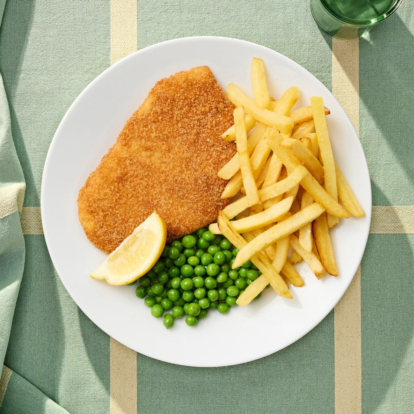 Rostlinný bezmasý řízek na talíři s hranolkami, hráškem a kouskem citronu.