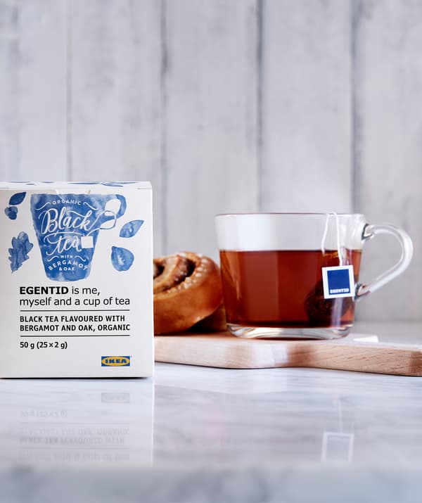Rotolo di cannella e tè in tazza di vetro su un piccolo vassoio, a sua volta posto su una sezione di piano di lavoro in marmo; pacchetto di tè a lato.