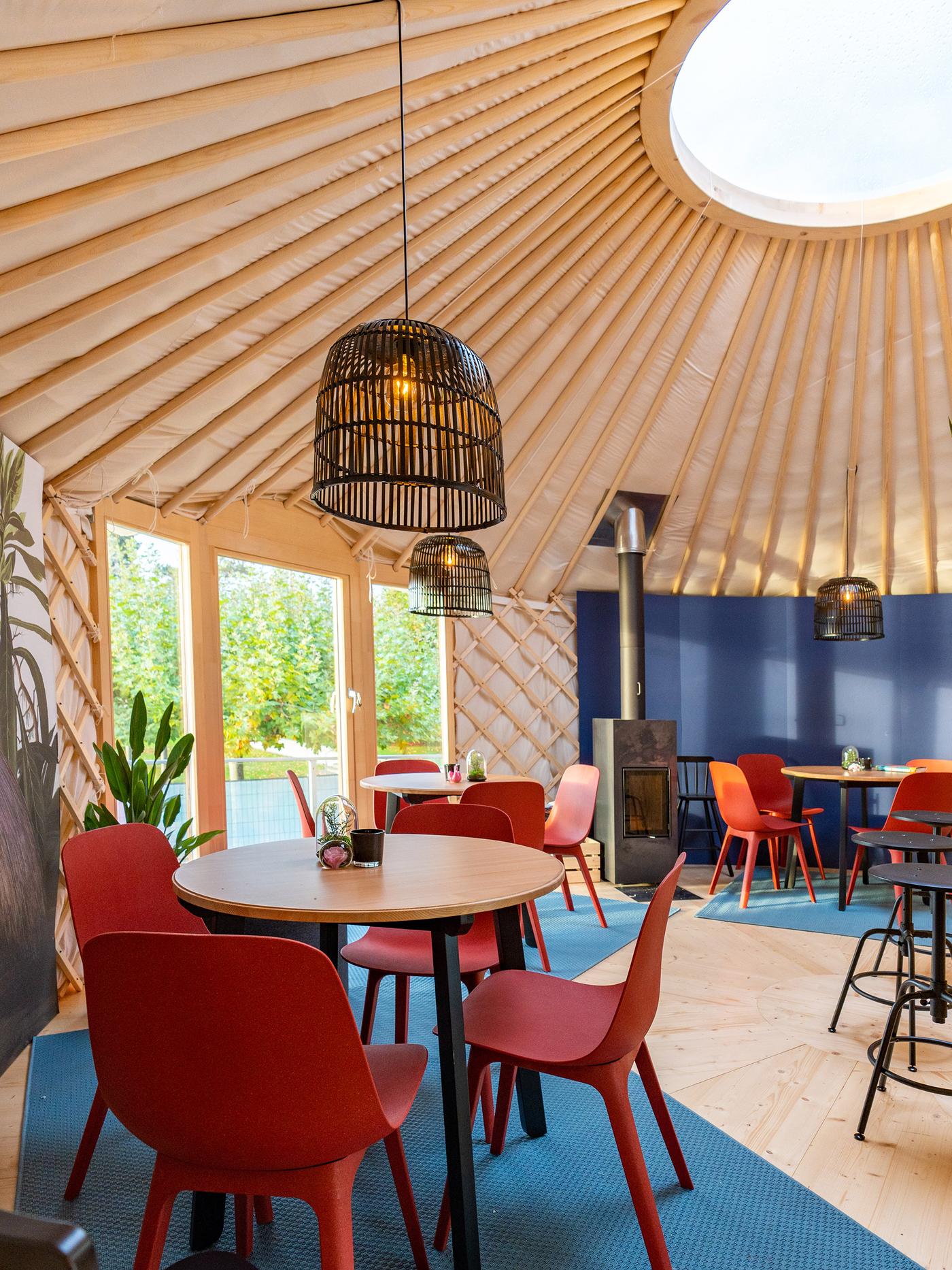 Round tables, each with four chairs, stand in a yurt with a large, glazed entrance door and a light well on the ceiling
