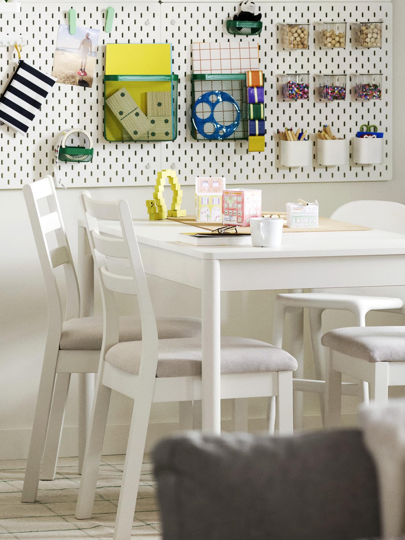 Rozkładany stół TONSTAD w kolorze złamanej bieli, otoczony czterema białymi krzesłami, ustawiony w jasnej jadalni ze schowkiem na ścianie.