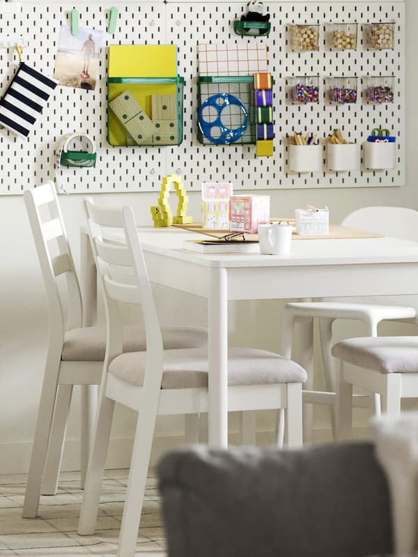 Rozkładany stół TONSTAD w kolorze złamanej bieli, otoczony czterema białymi krzesłami, ustawiony w jasnej jadalni ze schowkiem na ścianie.