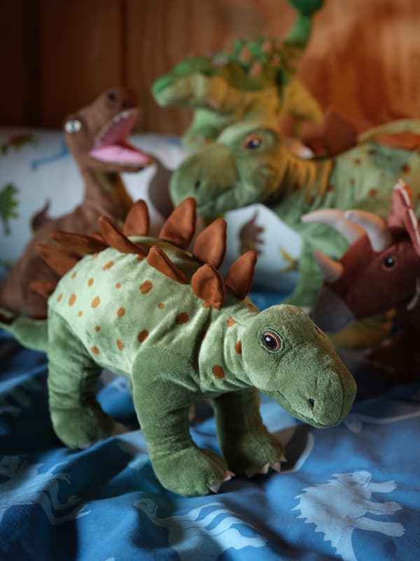 Rozličné dinosaury zo sortimentu plyšových hračiek JÄTTELIK na posteľných obliečkach so vzorom dinosaurov.