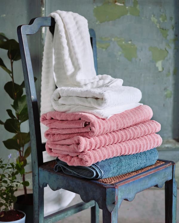 Rózsaszín, fehér és szürke, puha törülközők egy széken.