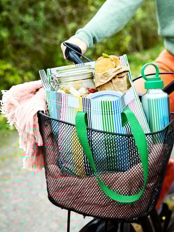 Rózsaszín HORNMAL takaró, egy ENKELSPÅRIG kulacs és egy teli FLADDRIG uzsonnás táska egy kerékpár tárolókosarában. 