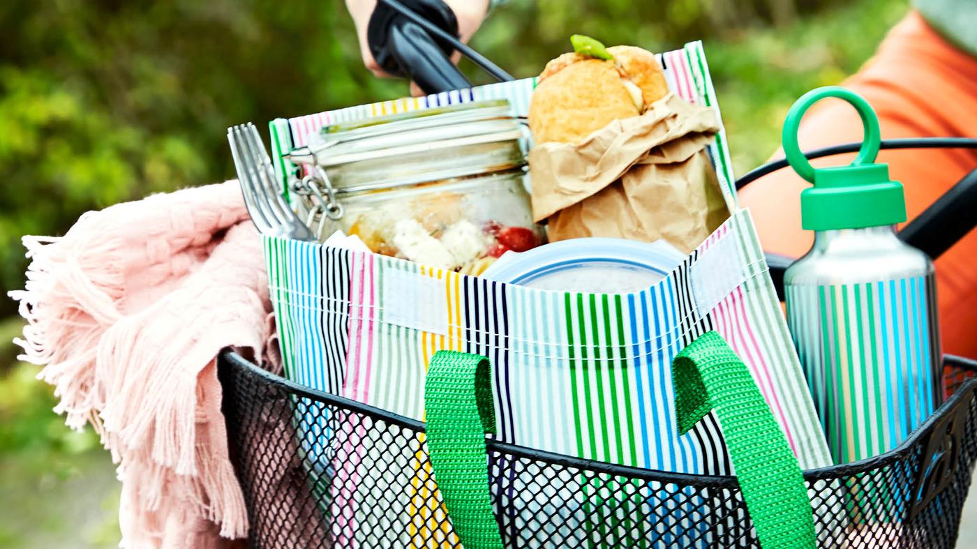 Rózsaszín HORNMAL takaró, egy ENKELSPÅRIG kulacs és egy teli FLADDRIG uzsonnás táska egy kerékpár tárolókosarában. 