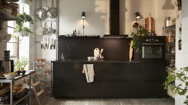 Ruang dapur dengan pintu kabinet dapur KUNGSBACKA IKEA berwarna hitam, troli keluli tahan karat dan dua lampu dinding berwarna hitam.