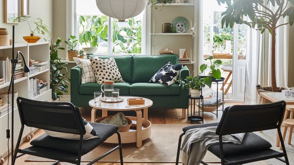 Ruang tamu cerah yang didominasi oleh sofa dua tempat duduk PÄRUP berwarna hijau gelap, tekstil corak grafik, serlahan kayu dan tumbuh-tumbuhan yang berdaun lebat.