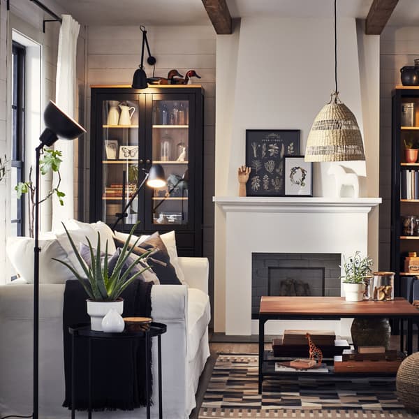 Ruang tamu dengan sofa berwarna putih, lampu dan meja sisi berwarna hitam, ambal bercorak berwarna kuning air dan dua meja kopi berwarna hitam/kayu.
