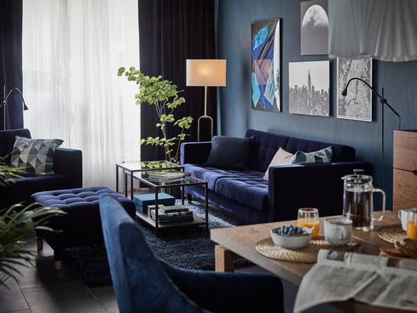 Ruang tamu yang mempunyai kerja seni, tumbuh-tumbuhan dan sofa LANDSKRONA berwarna biru gelap, bangku kaki dan kerusi berlengan di sekitar rangkaian meja VITTSJÖ.
