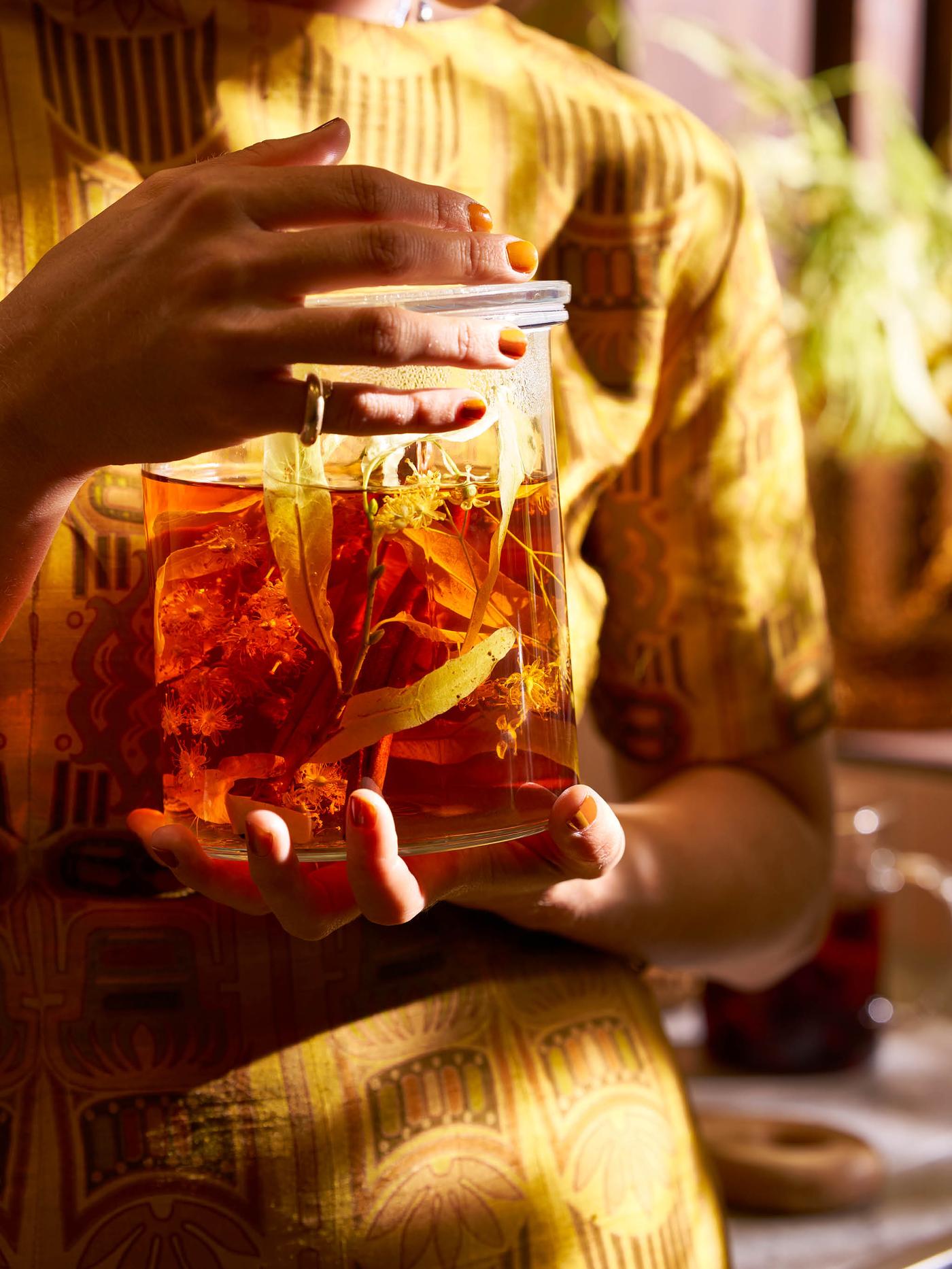 Ruce drží skleněnou dózu s víkem IKEA 365+ s bylinkovým čajem.