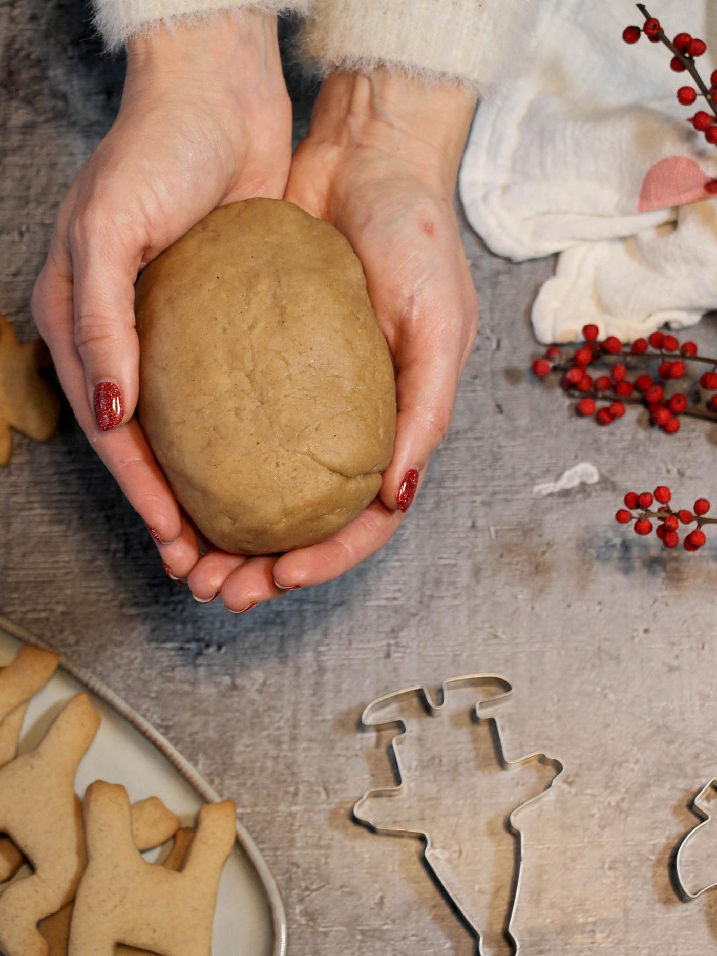 Ruce držící zpracované těsto na perníčky, vedle leží vykrajovátka VINTERFINT a upečené perníčky na talíři GLADFELIG, 