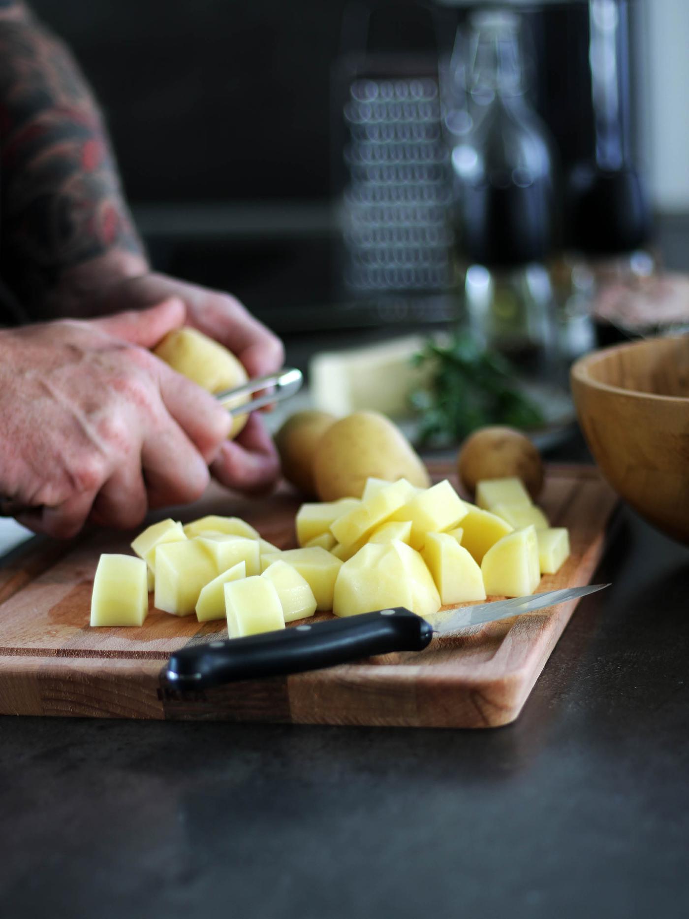 Ruce loupající škrabkou bramboru, další kousky brambor leží na prkénku PROPPMÄTT.