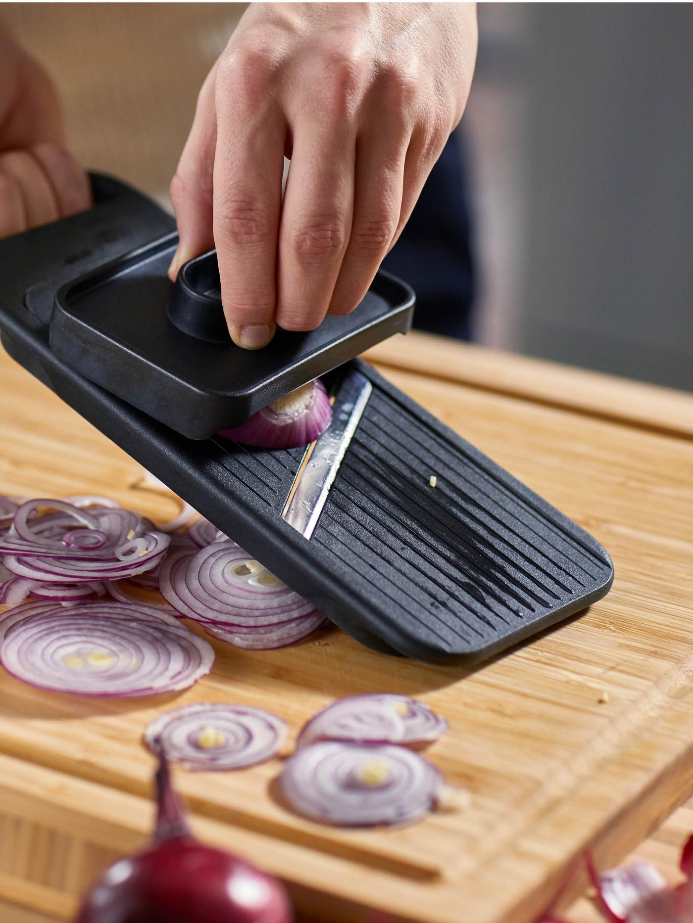 Ruce plátkují na kráječi na zeleninu IKEA 365+ červenou cibuli na prkénko APTITLIG.