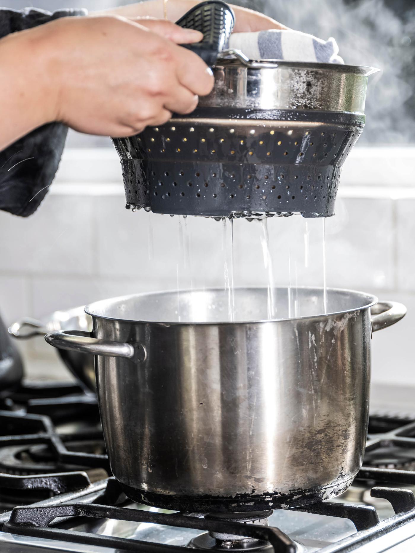 Ruce vytahují cedník KLOCKREN s těstovinami z hrnce OUMBÄRLIG.