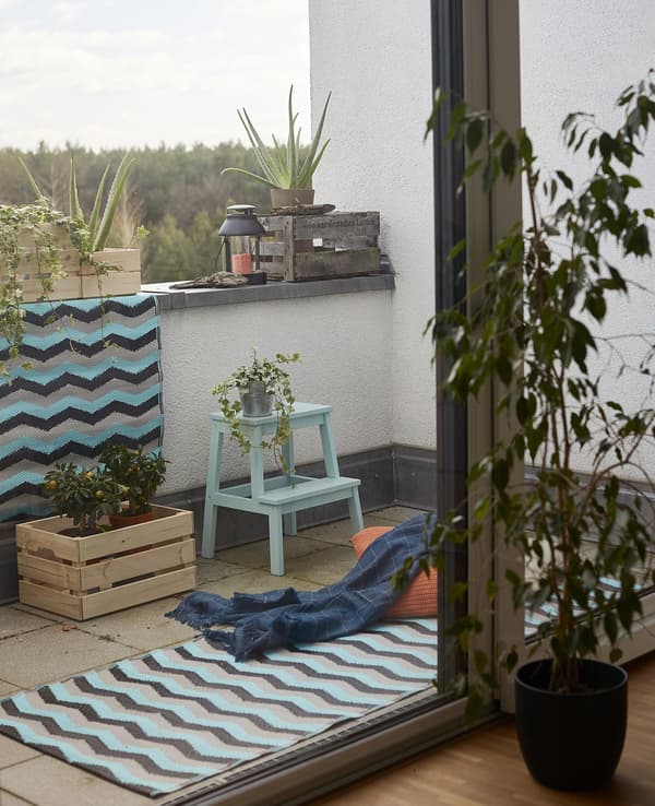 Rugs, throws, plants and crates on a balcony.