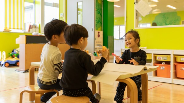 明るい室内で子どもたちがテーブルを囲み遊ぶ様子。カラフルな家具と自然光が差し込む空間。