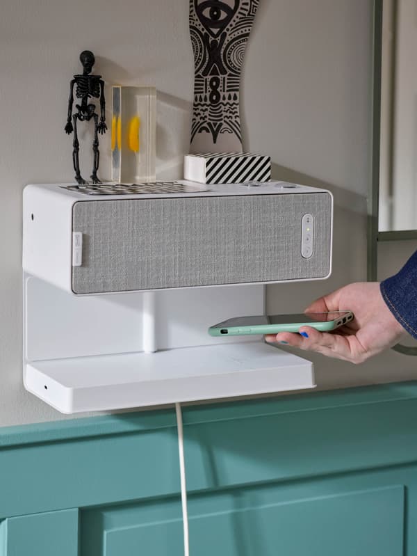 Ruka kladie mobilný telefón na zabudovanú nabíjačku v kombinácii reproduktora s policou SYMFONISK.