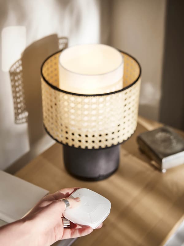 Ruka ovládá bílým dálkovým ovladačem lampu s Wi-Fi reproduktorem SYMFONISK.