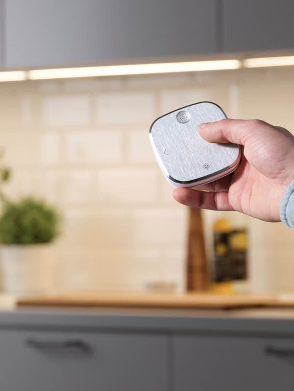 Ruka rozsvecuje svetlo v kuchyni pomocou diaľkového ovládača STYRBAR z nehrdzavejúcej ocele.