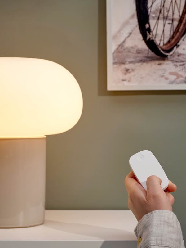Ruka s diaľkovým ovládačom TRÅDFRI rozsvecuje stolovú lampu DEJSA.