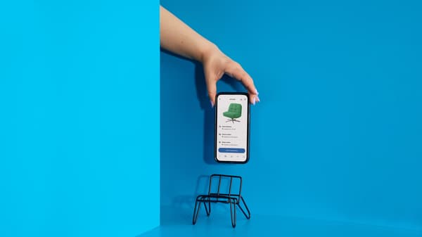 ruka s telefónom na modrom pozadí, s malou stoličkou pre telefón.