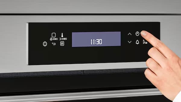 Ruka se chystá stisknout jedno z tlačítek na mikrovlnné troubě.