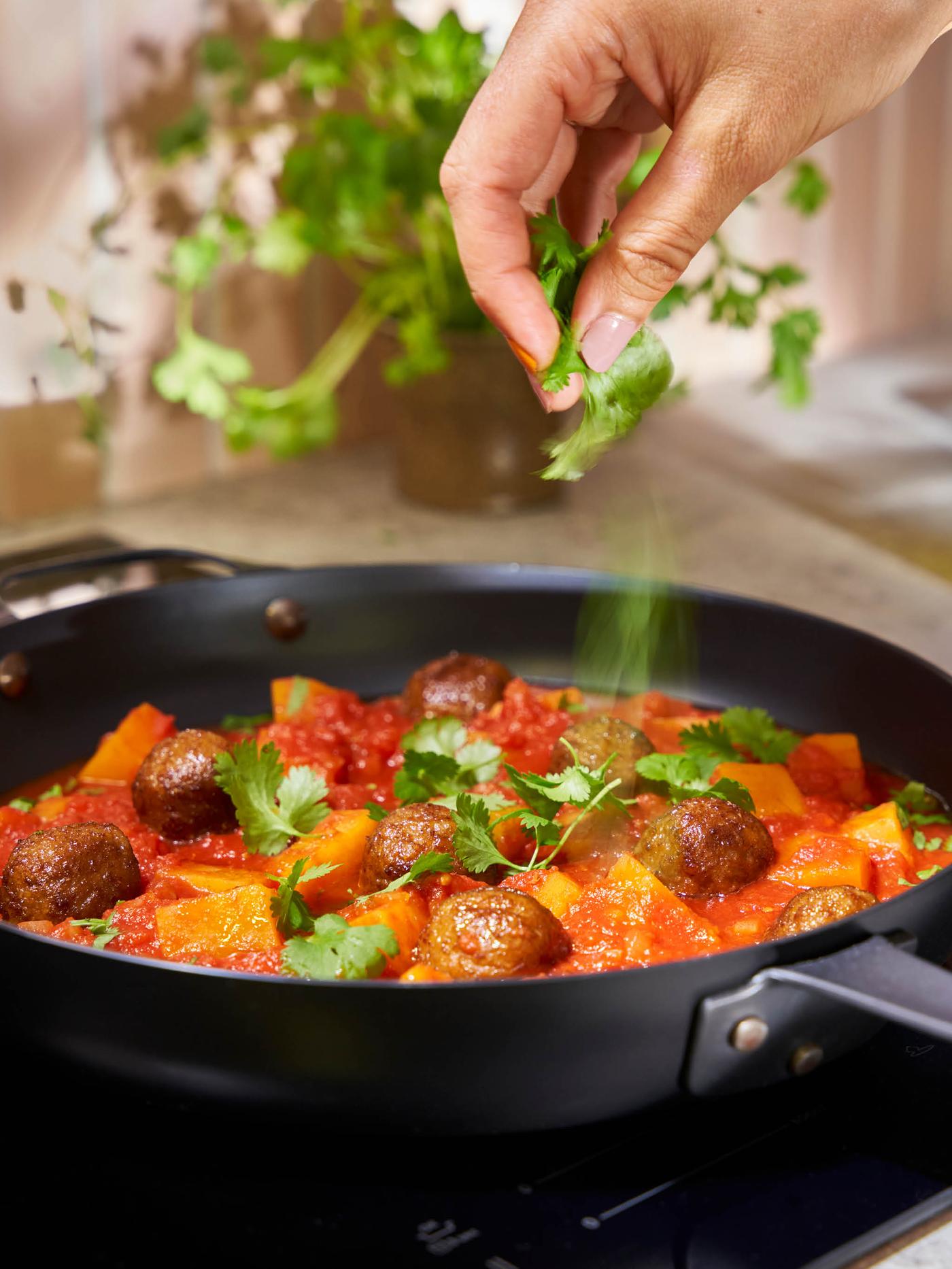 Ruka sype nakrájený čerstvý koriandr na dýňovo-rajčatový krém s bezmasými kuličkami na pánvi VARDAGEN.