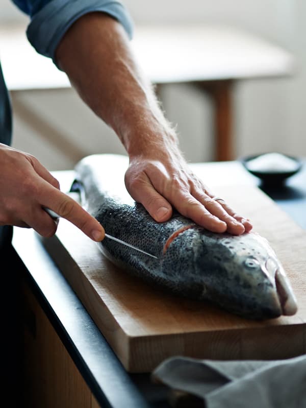 Ruky porcujú lososa na doske.