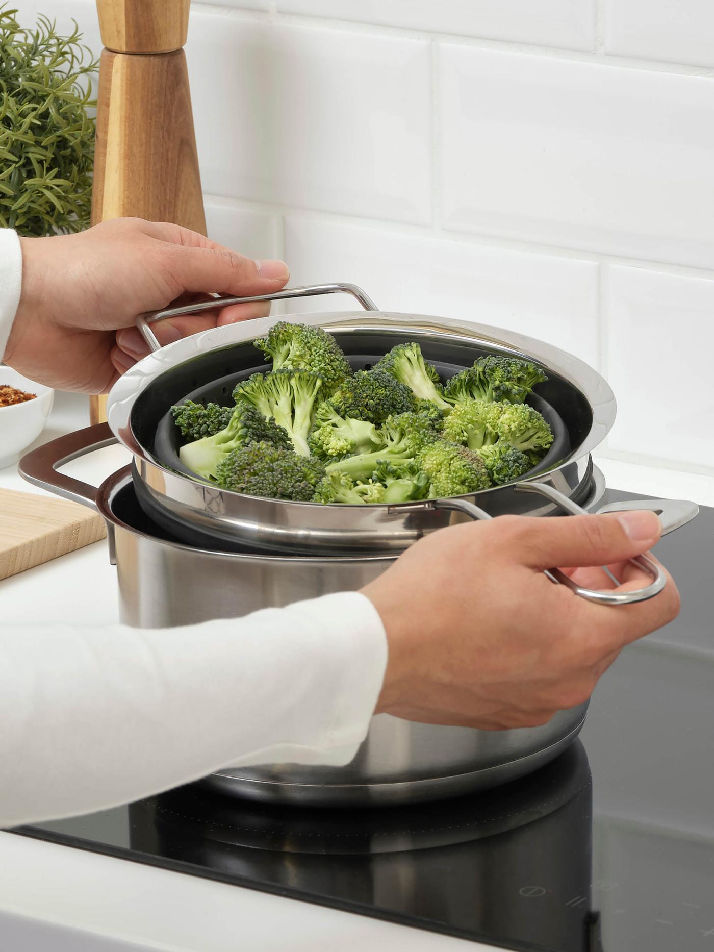 Ruky vyťahujú cedidlo KLOCKREN plné brokolice z hrnca HEMKOMST.