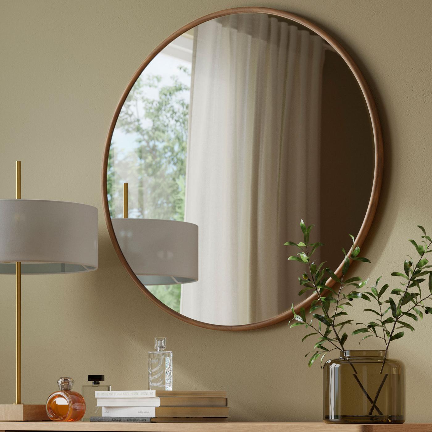 Rund spegel med valnötsram ovanför sminkbord i trä vid beige vägg.
