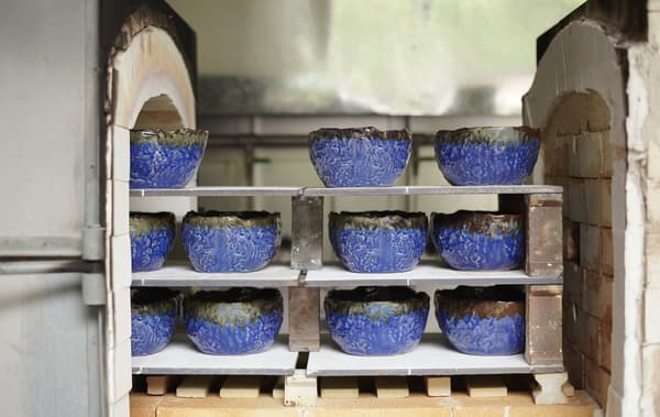 Rustic blue bowls on shelves of a brick kiln.