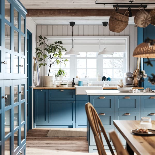 Rustic kitchen with blue cabinets, farmhouse sink under window, pendant lights, wood countertops, and cozy breakfast setup.