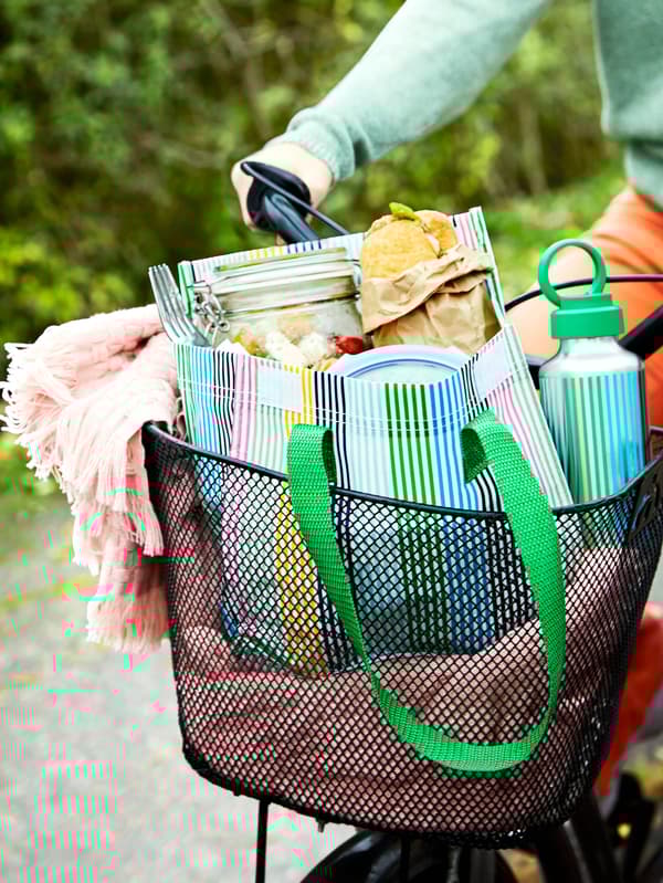 Ružová deka HORNMAL, fľaša na vodu ENKELSPÅRIG a plná taška na obedy FLADDRIG sú v koši na bicykli.
