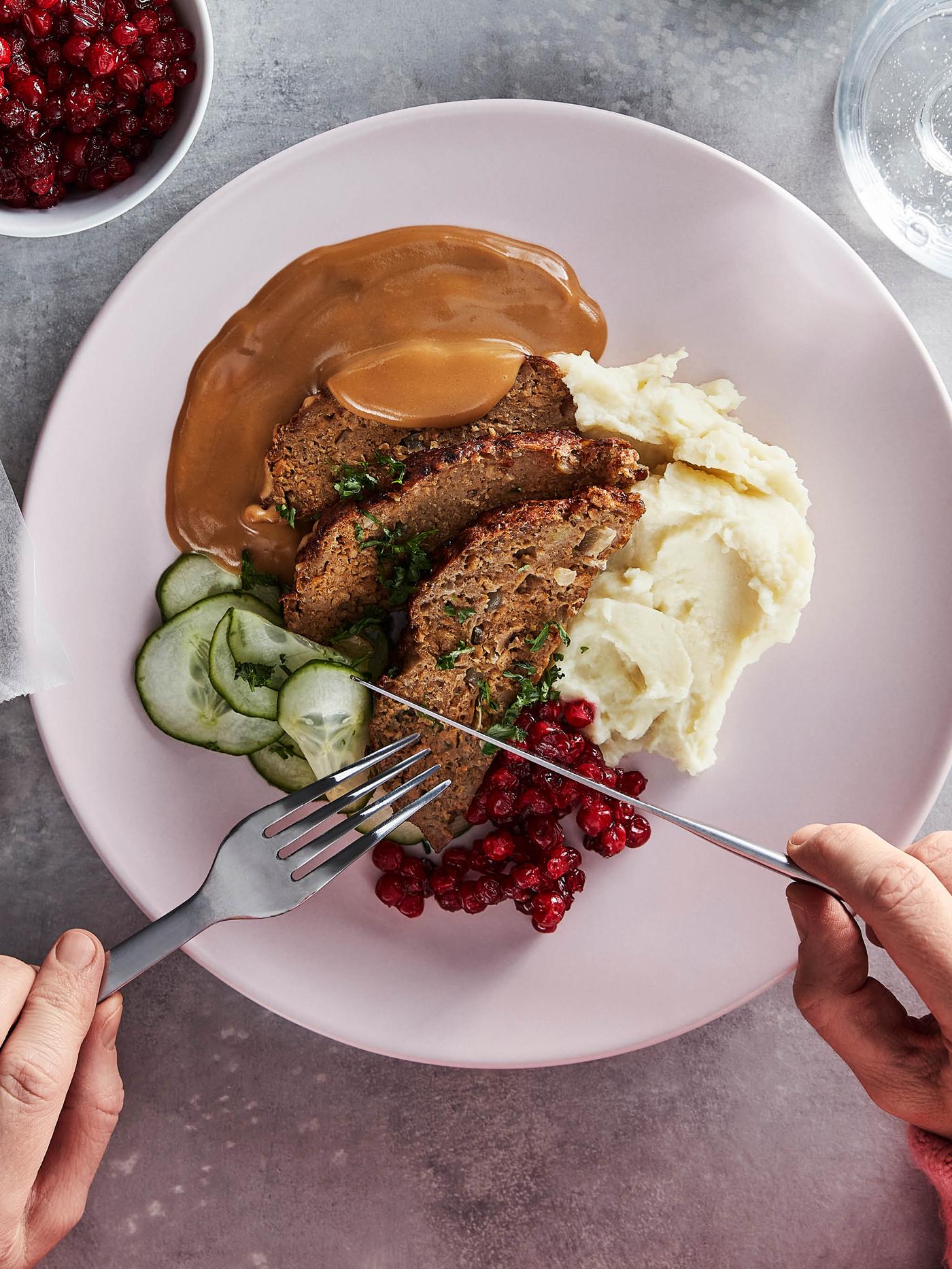 Růžový talíř se sekanou z bezmasé směsi VÄRLDSKLOK přelitou smetanovou omáčkou, bramborovou kaší, brusinkami a nakládanými okurkami.