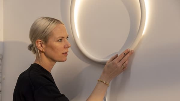 Sabine Marcelis qui regarde une applique à LED blanc métal de la collection VARMBLIXT 