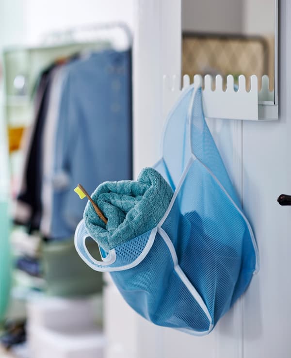 Sac en filet bleu avec serviette et brosse à dents, accroché à un crochet du miroir GARNES.
