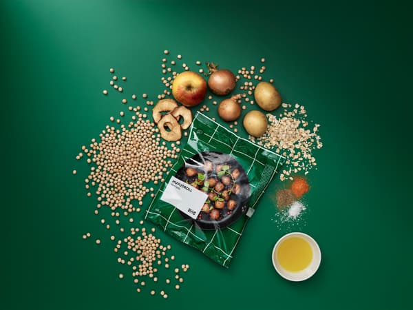 Sáček s bezmasými kuličkami HUVUDROLL, vedle jsou nezpracované ingredience: hrášek, oves, brambory, cibule, jablka a koření.