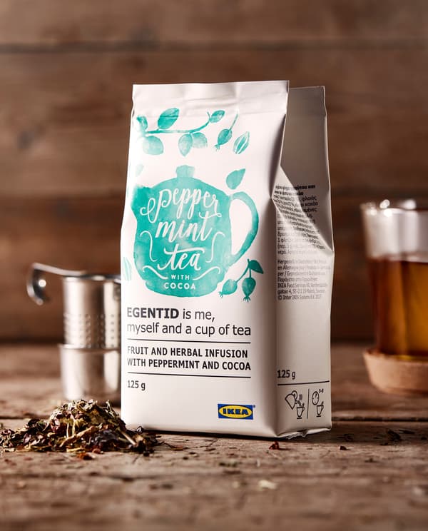 Sachet d’infusion de plantes placé sur un plan de travail en bois et entouré d’un kit pour faire du thé et d’une tasse de thé.